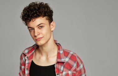 Ekose gömlek ve tank üst gri arka plan üzerinde kamera bakarak kıvırcık genç Portresi  