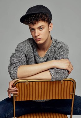 Siyah şapkalı yakışıklı erkek model ve stüdyoda sandalyede poz örgü süveter