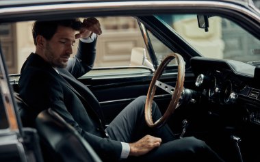 Eski arabada oturan siyah takım elbiseli yakışıklı adam