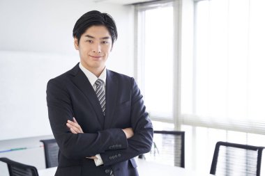 Japon bir erkek işadamı konferans odasında kollarını kavuşturuyor.