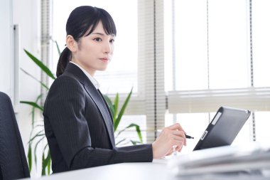 Ofisinde kağıt belgeleri veriye dönüştürmek için tablet kullanan bir Japon kadın.