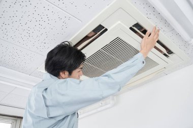 Japon bir erkek elektrikçi, ticari bir klimada bakım yapıyor.