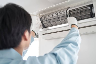 Japon bir erkek elektrikçi, klima filtrelerini kontrol ediyor.
