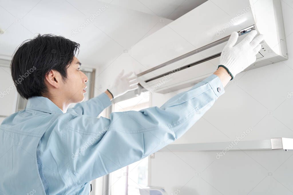 A Japanese male electrician installing a home air conditioner