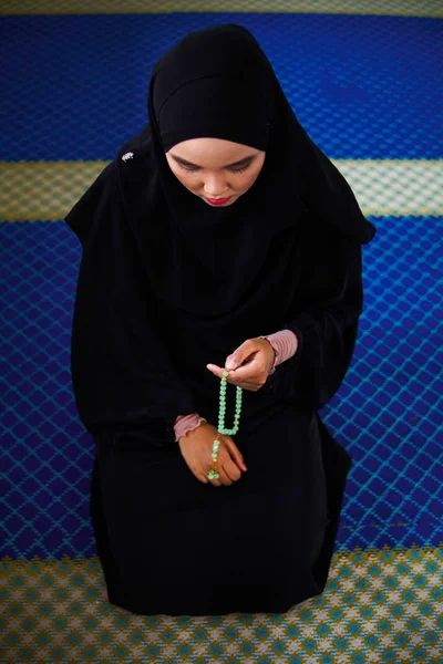 Young muslim woman praying, dzikir to Allah while holding a prayer beads inside a mosque