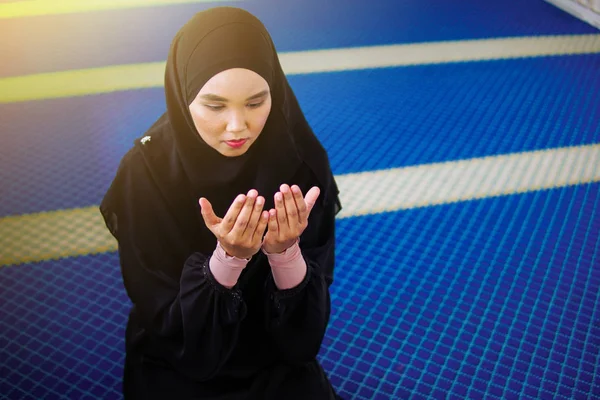 Young muslim woman praying to Allah with hands up inside a mosque