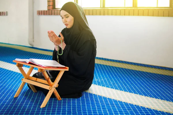 Young muslim woman praying to Allah with hands up on praying mat, holding beads