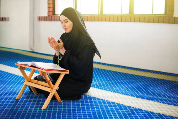 Mujer musulmana joven rezando a Allah con las manos en alto en la alfombra de oración, sosteniendo cuentas —  Fotos de Stock