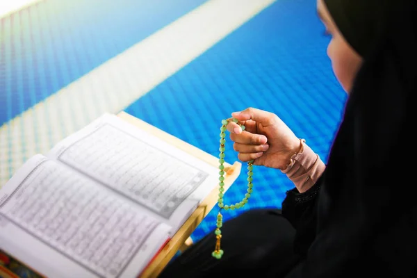 Pandangan samping wanita muslim muda dzikir kepada Allah di tikar doa dengan tangan memegang manik-manik di dalam masjid — Stok Foto
