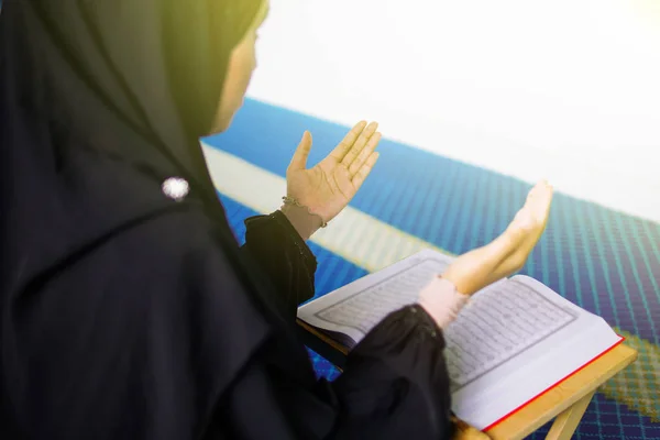 Young muslim woman praying to Allah with hands up in front of The Holy Quran inside a mosque — Stock Photo, Image