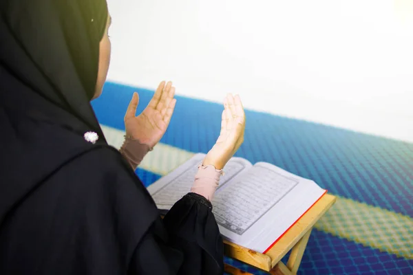 Mujer musulmana joven rezando a Allah con las manos en alto delante del Sagrado Corán dentro de una mezquita —  Fotos de Stock