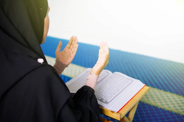 Allah 'a dua eden genç müslüman bir kadın. Kutsal Kur' an 'ın önünde bir caminin içinde elleri havada dua ediyor.