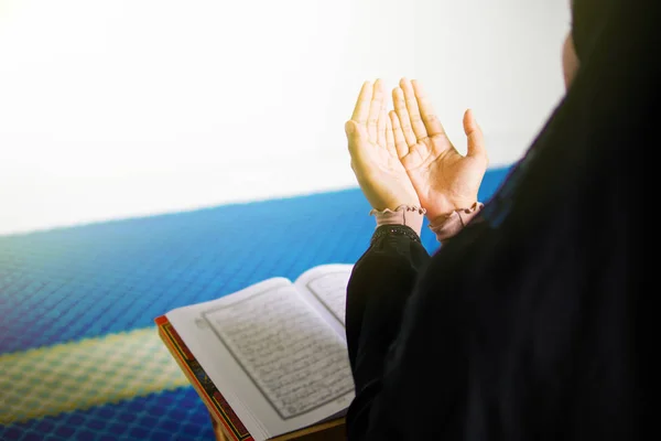 Young muslim woman praying to Allah with hands up in front of The Holy Quran inside a mosque
