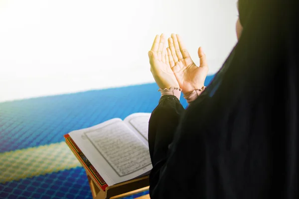 Jovem mulher muçulmana orando a Deus com as mãos para cima na frente do Alcorão dentro de uma mesquita — Fotografia de Stock