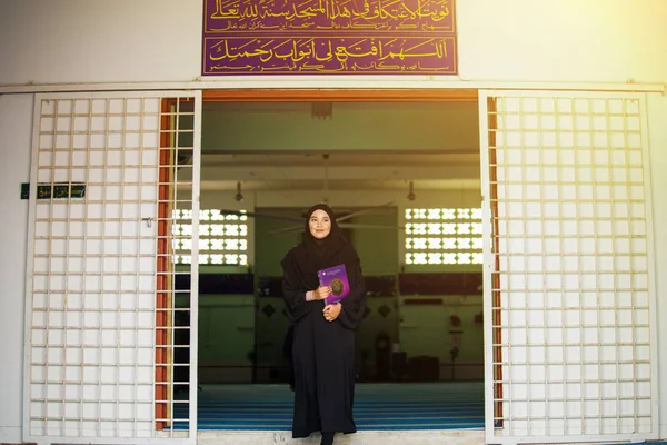 Siyah abaya elbisesi giyen genç Müslüman kadın, Kuran 'ı bir caminin içinde tutuyor. — Stok fotoğraf