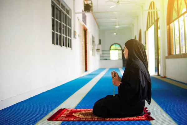 Vista lateral de la joven musulmana dzikir a Allah en la alfombra de oración con la mano sosteniendo cuentas dentro de una mezquita — Foto de Stock