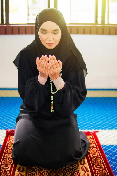 Mujer musulmana joven rezando a Allah con las manos en alto en la alfombra de oración, sosteniendo cuentas —  Fotos de Stock