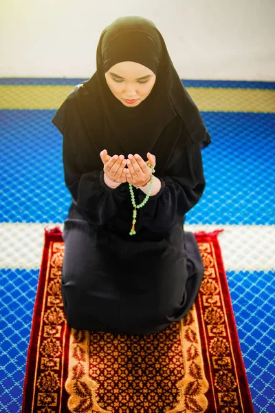 Junge muslimische Frau betet zu Allah mit erhobenen Händen auf Gebetsmatte und hält Perlen in der Hand — Stockfoto