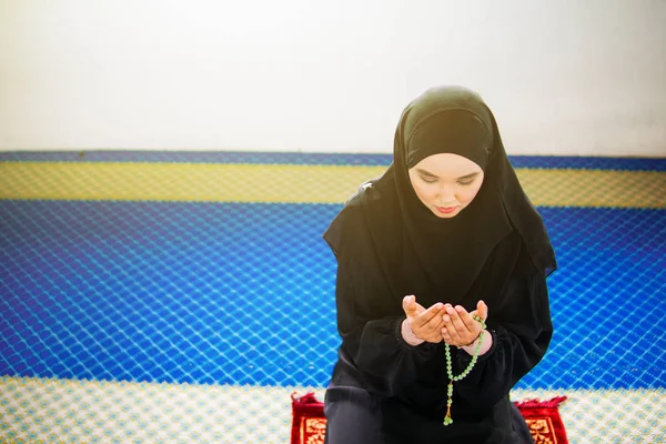 Mujer musulmana joven rezando a Allah con las manos en alto en la alfombra de oración, sosteniendo cuentas — Foto de Stock