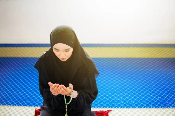 Giovane donna musulmana che prega Allah con le mani alzate sul tappeto di preghiera, tenendo perline — Foto Stock