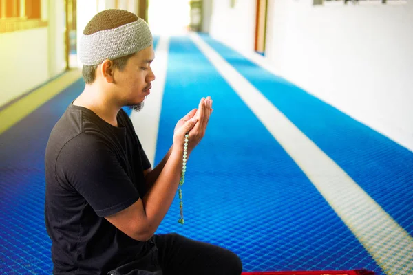 Vista laterale dell'uomo musulmano che fa du 'a mentre tiene perline che pregano sul tappeto di preghiera all'interno di una moschea — Foto Stock