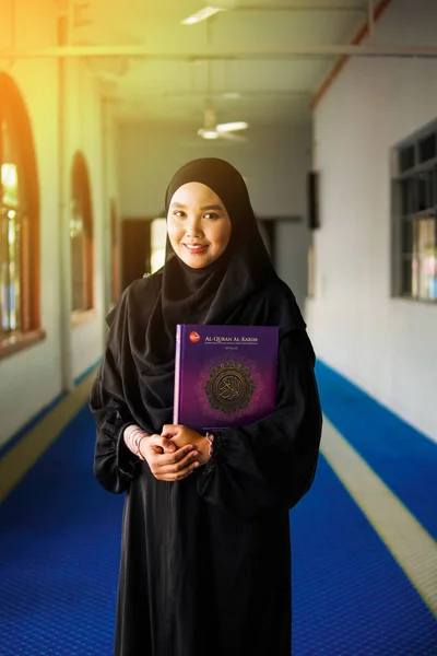 年轻的穆斯林妇女穿着黑色的阿巴雅衣服，在清真寺里拿着《古兰经》 图库图片