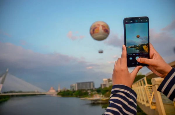 Bir kadın bir cep telefonu kullanarak gökyüzüne uçan bir sıcak hava balonu bir resim alıyor
