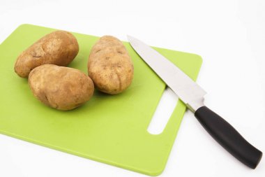 Beyaz arka plan ile yeşil bir kesme tahtası üzerinde bir bıçak ve russet patates üst görünümü.