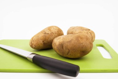 Beyaz arka planlı yeşil bir kesme tahtası üzerinde bir bıçak ve russet patates görünümü ne kadar yakın.