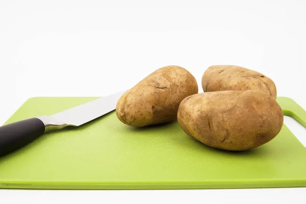 Beyaz arka planlı yeşil bir kesme tahtası üzerinde bir bıçak ve russet patates görünümü ne kadar yakın.