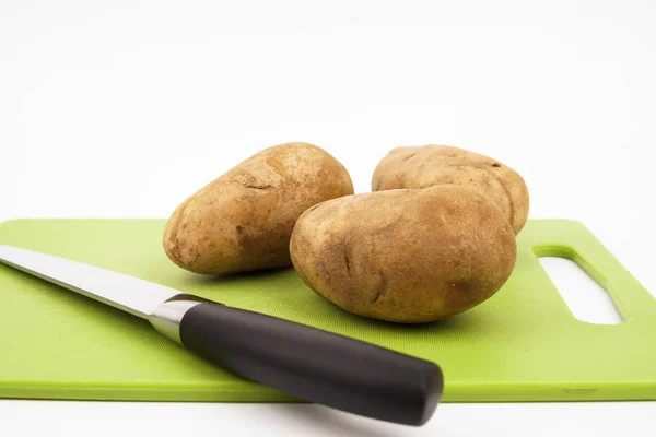 Close-up vista de uma faca e batata russet em uma placa de corte verde com fundo branco . — Fotografia de Stock