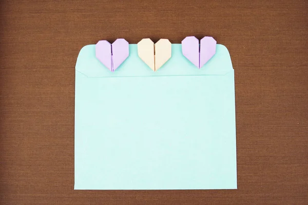 Une enveloppe bleue et un coeur en papier origami sur fond de texture bois. Concept de pose plate . — Photo