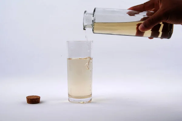 Uma mão despeje uma garrafa de água suja em um copo cheio de água limpa no fundo branco — Fotografia de Stock