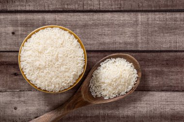 Pişmemiş kuru Tayland yasemin pilavı kasede ve ahşap kepçe yanında izole edilmiş ahşap zemin zemin zemin zemin, düz yatay ve üst yatay manzara.