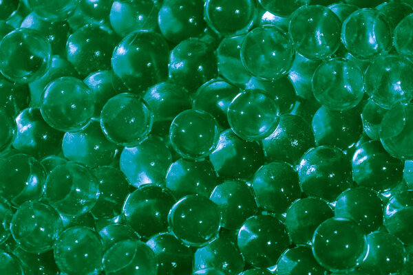 Transparent green hydrogel balls. Green water gel balls with bokeh. Polymer gel Silica gel. Liquid crystal ball with reflection. Green balls texture background