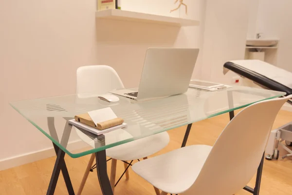 Wnętrze minimalistycznego biura z białymi ścianami, drewnianą podłogą, drewnianym i szklanym stołem komputerowym i białą bibliotą z folderami. Sala konsultacja fizjoterapii — Zdjęcie stockowe