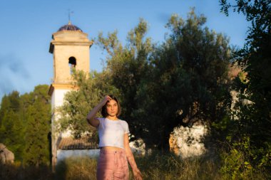 Genç kız kırsal ayakta, yüksek çim dokunmadan ve ileriye bakıyor.