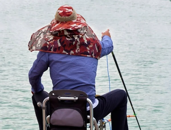 guy, man sits on a small special chair, throws the bait from the pier into the lake