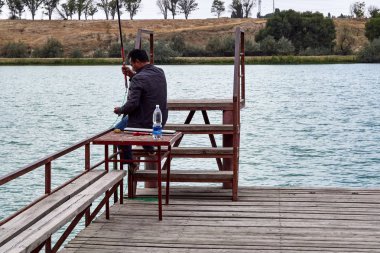 ayakları üzerinde adımları ile merdivenlerden yakınındaki bir iskelede balık yakalamak bir masada oturan Editör, Asya adam