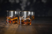 Silný alkohol, sklenice na whisky s ledem, stojí na tmavém starodávném dřevěném stolku a černém pozadí, kde je místo pro kopírování