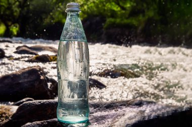 Doğanın arka planına karşı bir şişe taze, serin su, en saf su ile bir dağ nehri.