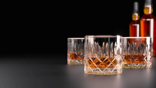 Güçlü alkollü içecekler, bardak ve bardak, viski, brendi varlığında. alkol bir şişe ile karanlık bir arka plan üzerinde, seçici dikkat ve hafif tavlama ile