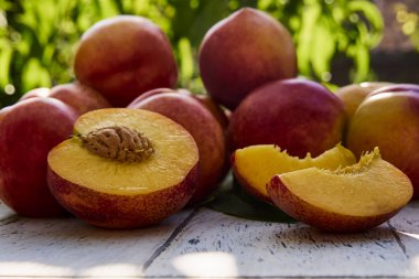 Yeşil yaprakların arka planına karşı eski ahşap masada yaprakları ile olgun şeftali. Bahçede taze tatlı dilimlenmiş şeftali. Yumuşak seçici odaklama