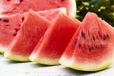 Taze olgun çizgili dilimlenmiş karpuz ahşap eski bir masa üzerinde, yeşil yaprakların arka planına karşı, açık havada.