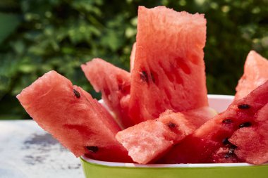 Taze olgun çizgili dilimlenmiş karpuz ahşap eski bir masa üzerinde, yeşil yaprakların arka planına karşı, açık havada.