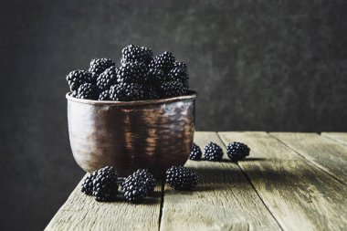 Koyu bir arka plan üzerinde eski ahşap tahtalar üzerinde eski bakır yemekler olgun böğürtlen.