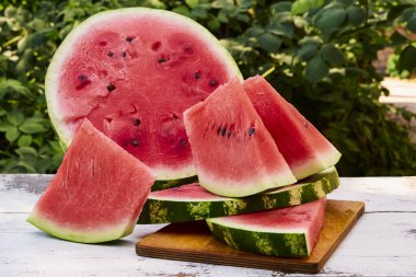 Taze olgun çizgili dilimlenmiş karpuz ahşap eski bir masa üzerinde, yeşil yaprakların arka planına karşı, açık havada.