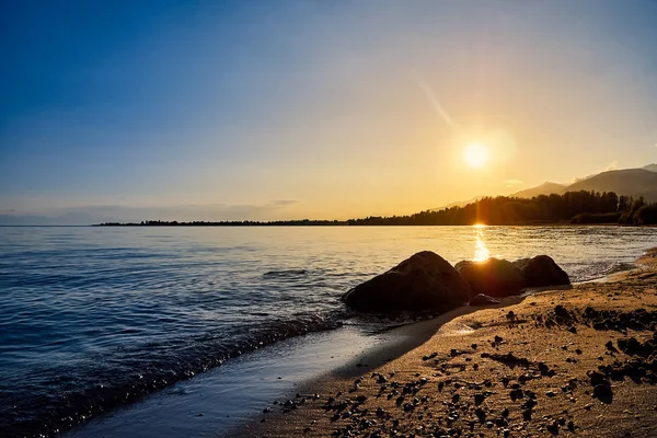 Gün batımında taşlarla plajın güzel manzarası, dağların arka planında akşam güneş ışığı ile aydınlatılmış, lüks yaz maceraları, açık hava etkinlikleri, yürüyüş