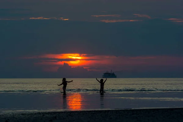 Siluet siyah gölge suya yakın oynayan çocuklarda Coast, dramatik gökyüzü kara bulut günbatımı su arka planda üzerinde plaj