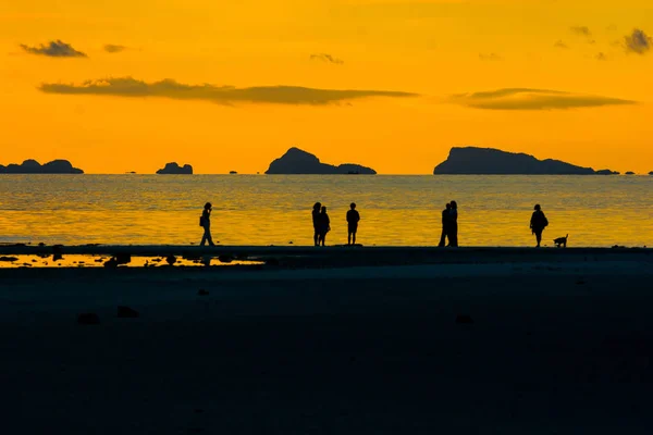 SILHOUETTE PEOPLE TAKING A WALK ON SAND BANK AT SEASIDE IN EVENING TIME , GOLDEN SKY LIGHT CLOUD OVER ISLAND AND OCEAN BACKGROUND